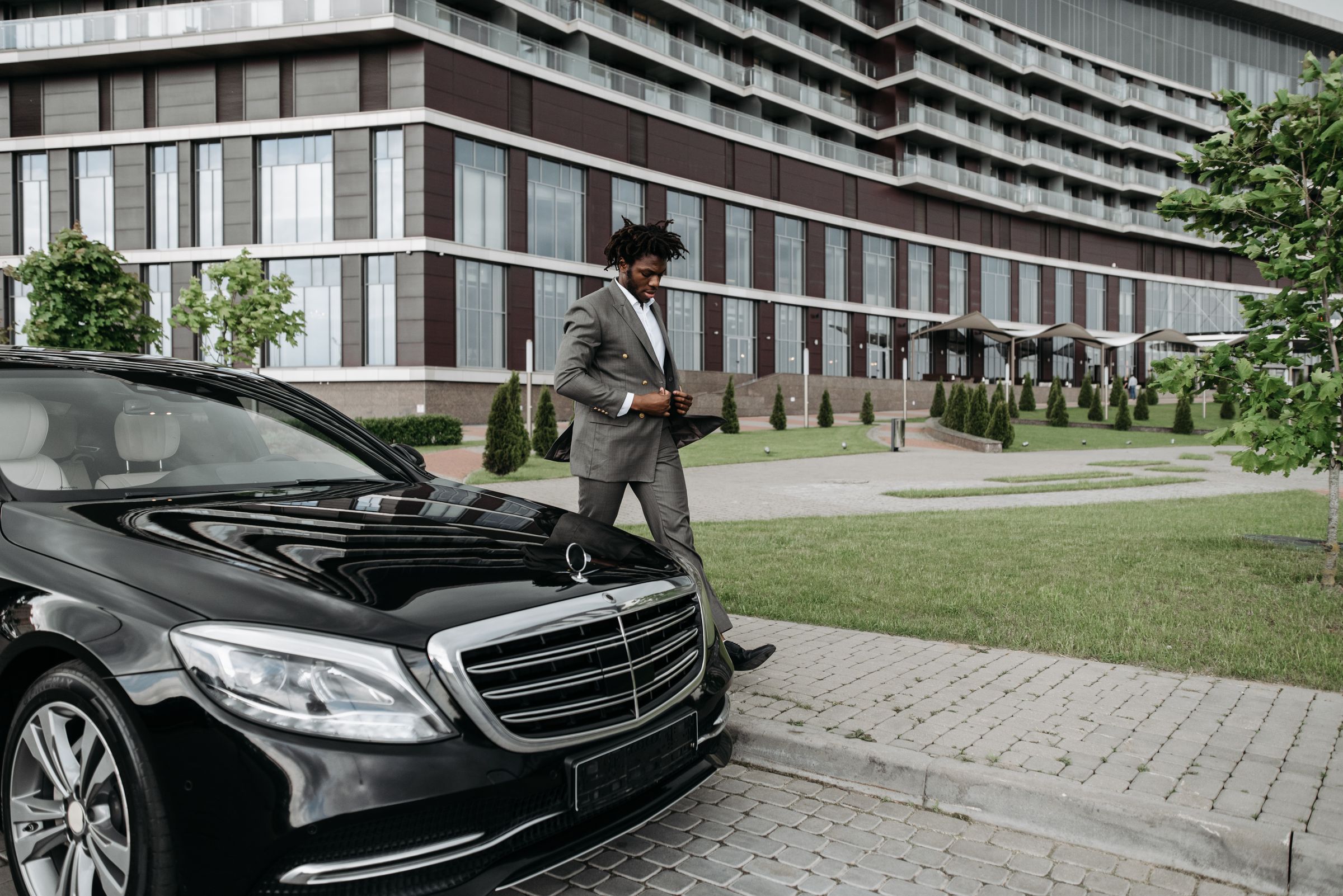 Professional Ghanaian executive chauffeur standing beside a premium fleet vehicle outside a modern institutional facility, discreet luxury, operational professionalism